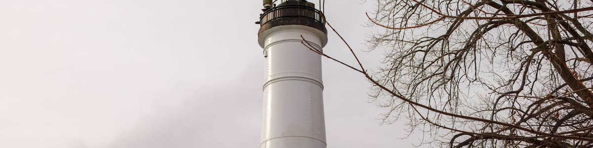 A tall white lighthouse with a mural on the adjacent wall, a bench, and a snow-covered ground.