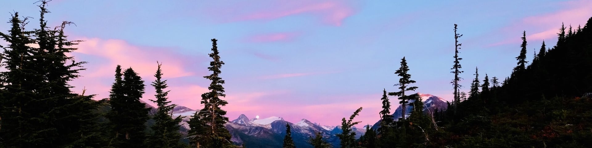 A forested mountain landscape with a sunset sky.