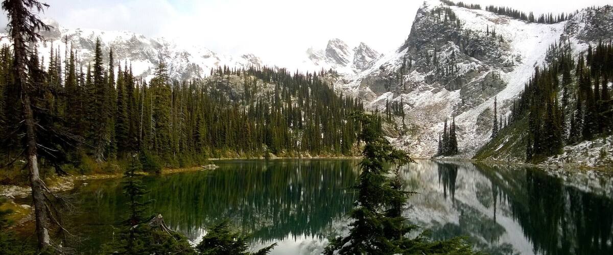 A serene mountain lake surrounded by dense evergreen forests and snow-capped peaks.