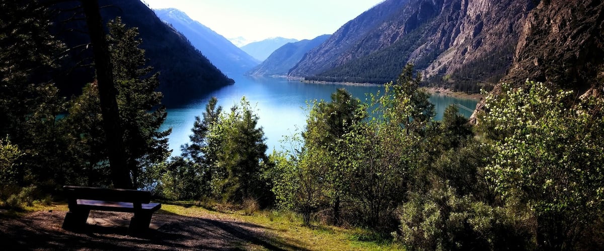 A bench overlooking a lake surrounded by mountains.