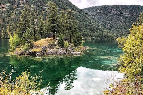 Ein klarer See, umgeben von dichtem Wald und Bergen.