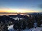 Un paysage de montagne enneigé au coucher du soleil, avec un lac et des zones boisées.