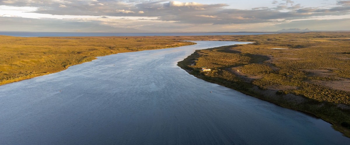 A river winding through a flat, open landscape with sparse vegetation and a distant mountain range.