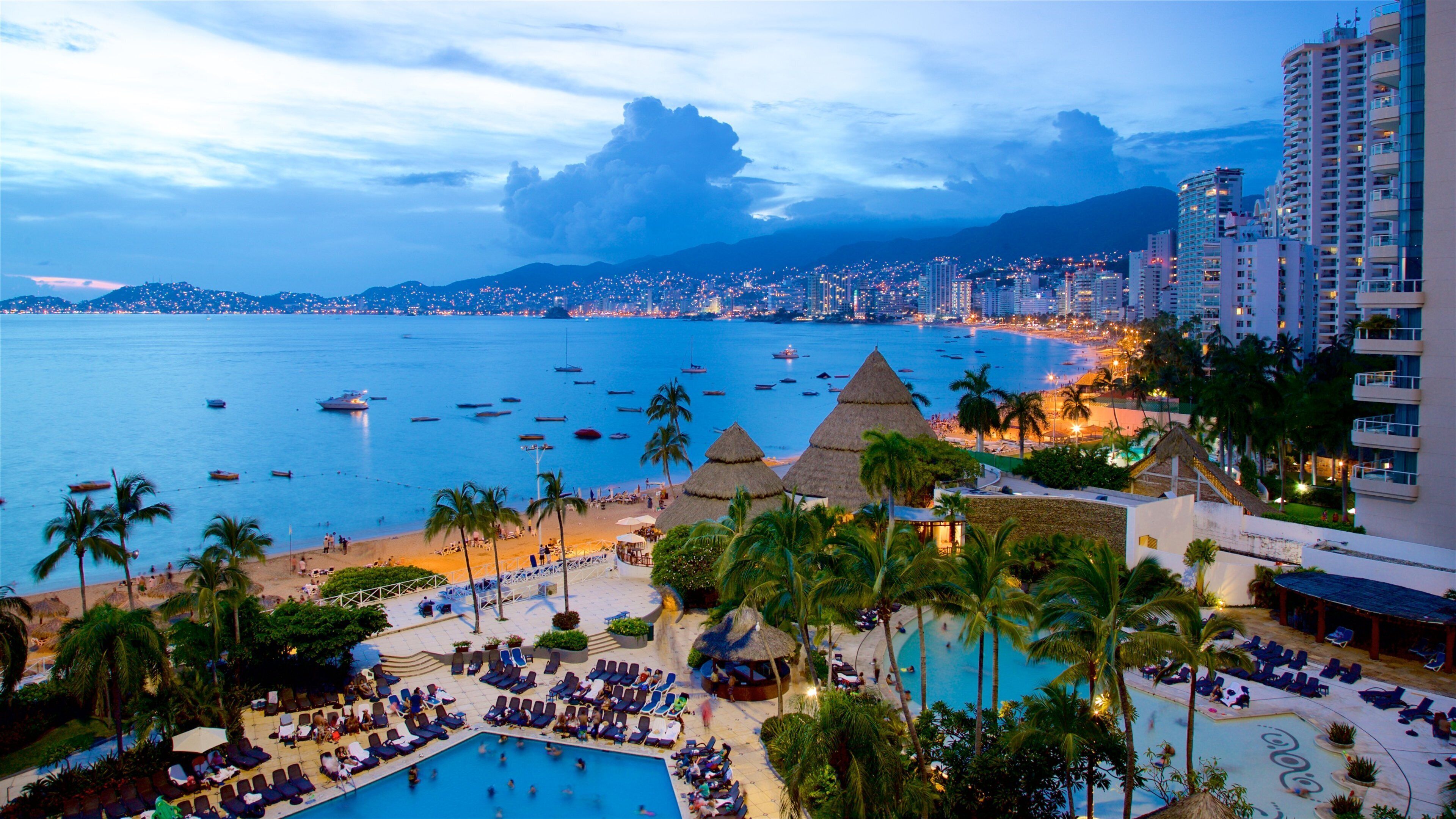 A resort with a pool, palm trees, and a beach with boats.