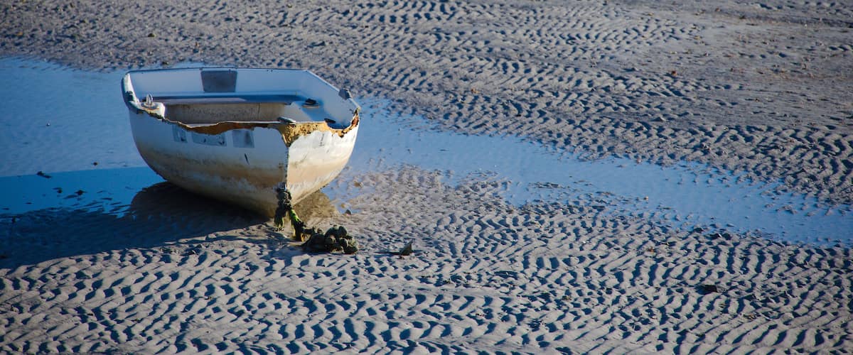 A lone Small White Boat Resting on Wet Sand with Ripples, a Shallow Pool, and Calm Beach Scene in Gulfport, FL. Low tide on damp sand next to a shallow tidal pool, creating a tranquil coastal scene wi