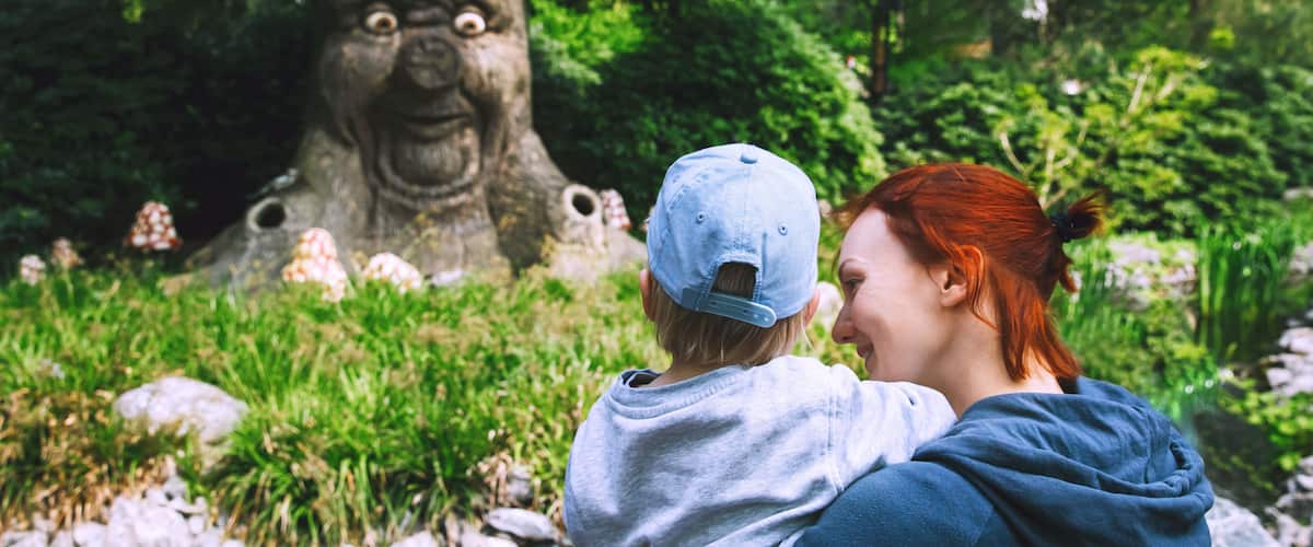 A person holding a child in front of a tree with a carved face.