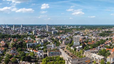 Aerial view of Eindhoven, Netherlands, featuring modern high rises, red tiled residential areas, tree lined streets, and a flat horizon under a blue sky.