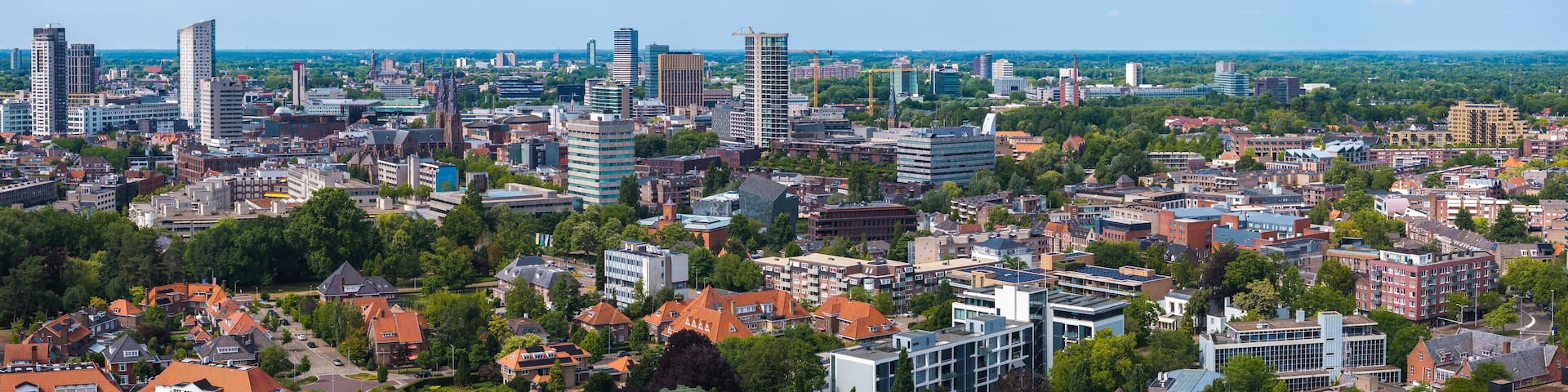 Aerial view of Eindhoven, Netherlands, showcasing skyscrapers like Vesteda Tower, traditional structures, greenery, and construction cranes under a blue sky.
