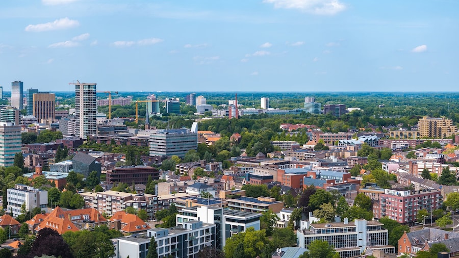 Aerial view of Eindhoven, Netherlands, showcasing skyscrapers like Vesteda Tower, traditional structures, greenery, and construction cranes under a blue sky.