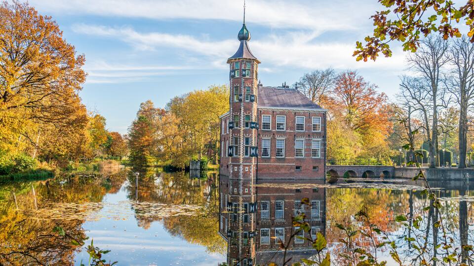 A historic building with a tower, a canal, and autumn foliage.