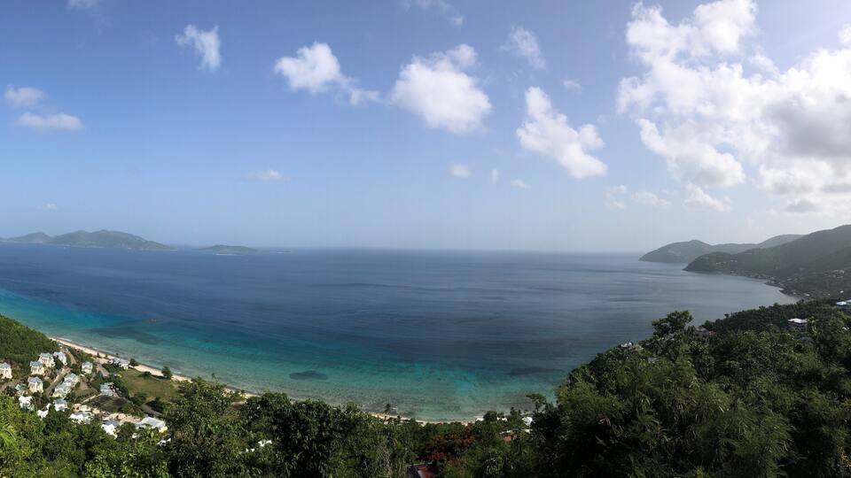 A coastal landscape with a clear view of the ocean, a beach, and surrounding hills.