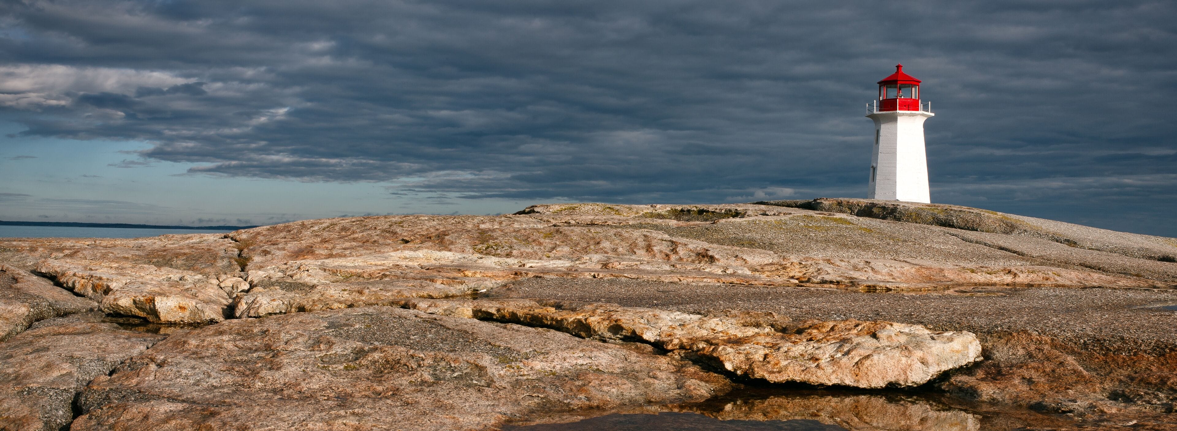A white lighthouse with a red top on a rocky outcrop.