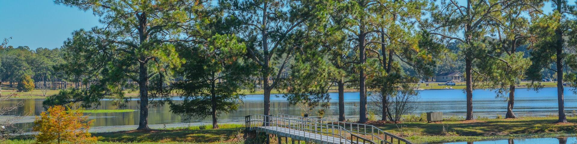 A bridge over a lake with trees and a clear blue sky.