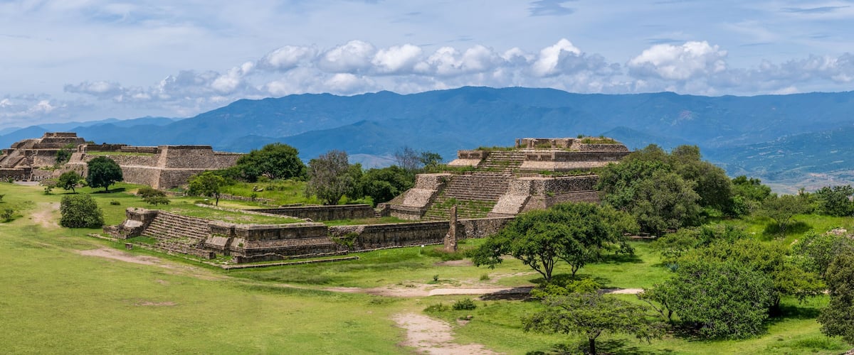 Ancient Mayan ruins with terraced structures and a mountainous backdrop.