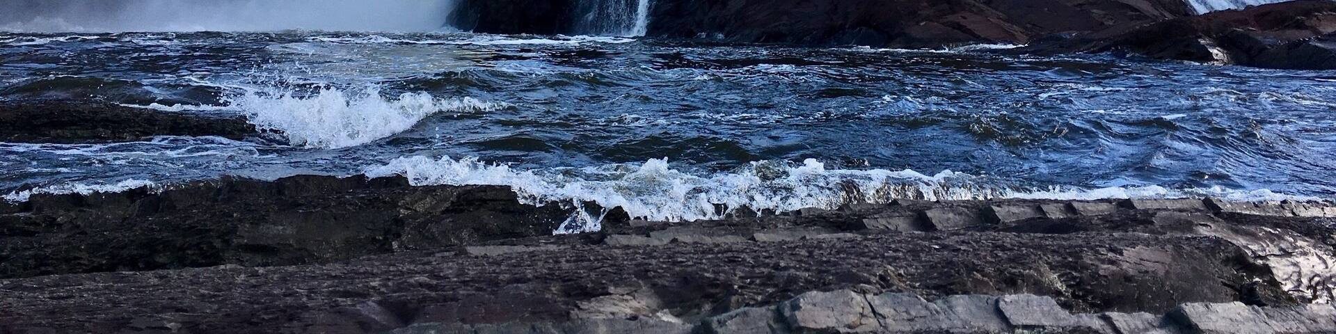 A powerful waterfall cascading over rocky cliffs into a turbulent river.