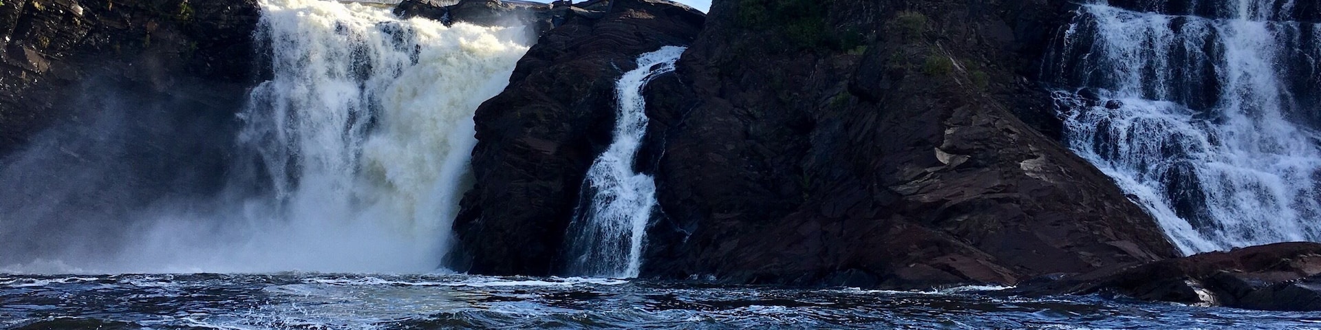 Una cascada imponente que se precipita sobre acantilados rocosos hacia un río turbulento.