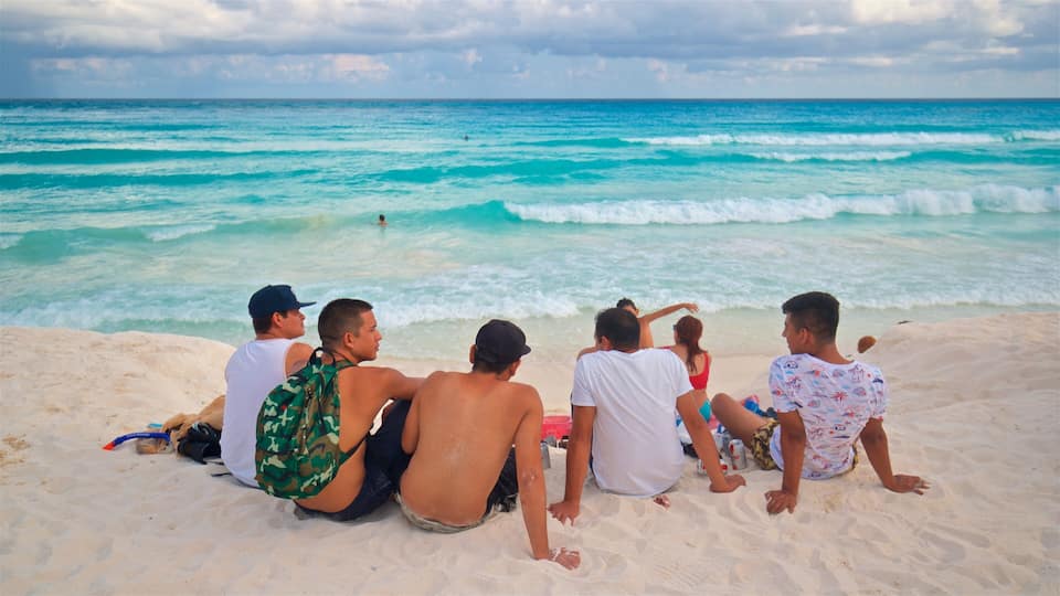 A group of people sitting on a sandy beach, facing the ocean.