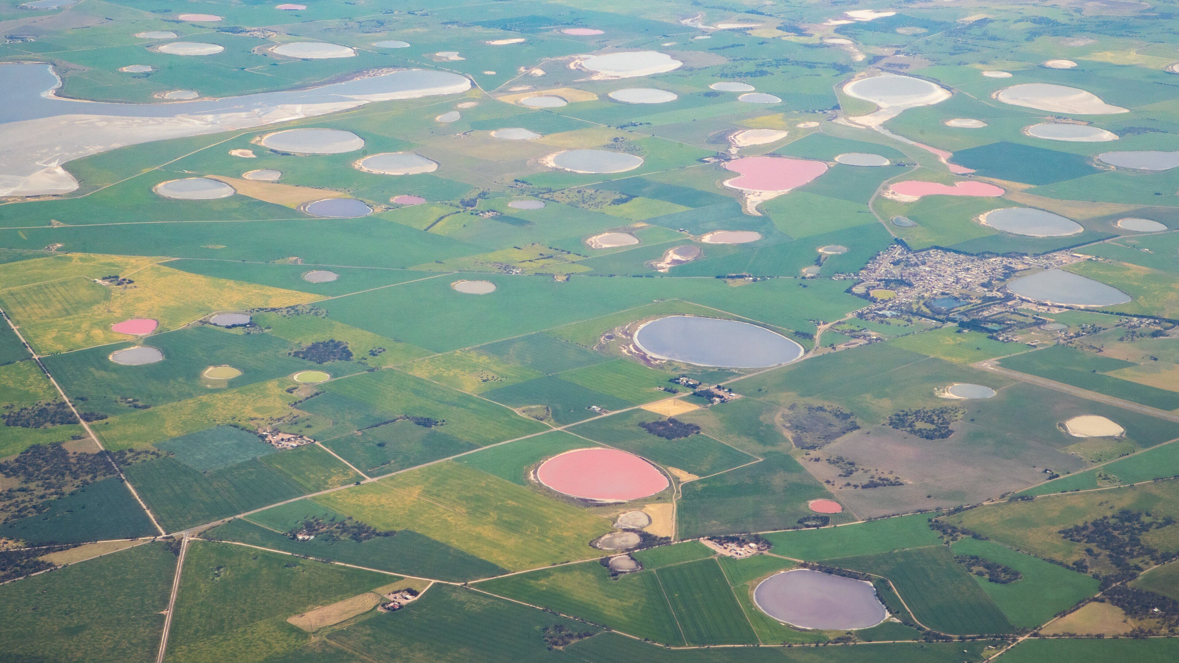 An aerial view of a landscape with numerous circular water bodies and green fields.