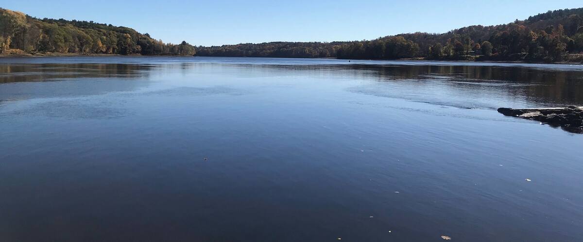 A calm lake with a dock in the foreground and forested hills in the background.