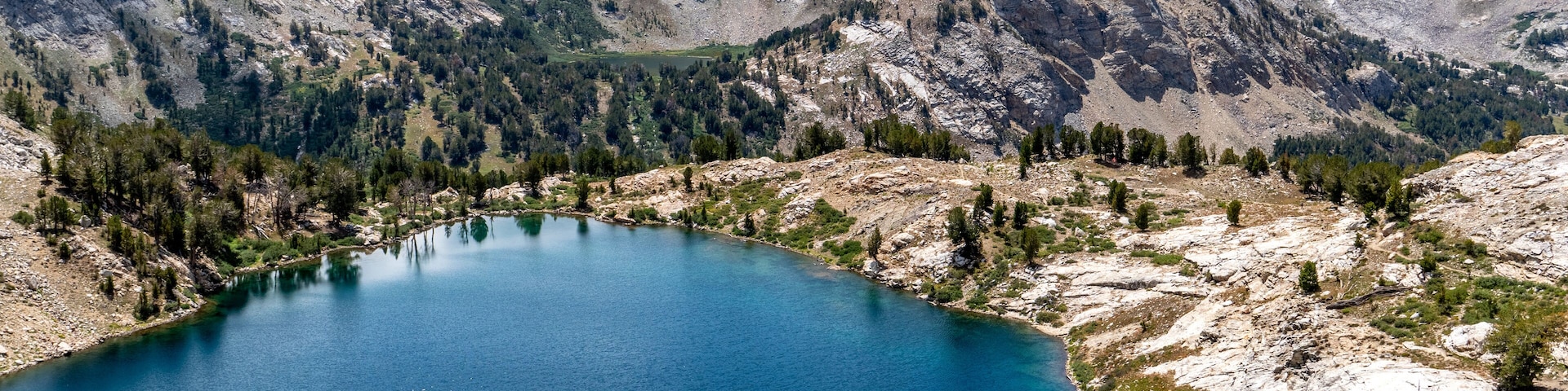 Man, hiker, standing, watching a scene of an alpine lake and rugged mountains with trees, rocks, and puffy clouds in the blue sky, Liberty Lake, Ruby Mountain Range, Elko, Nevada