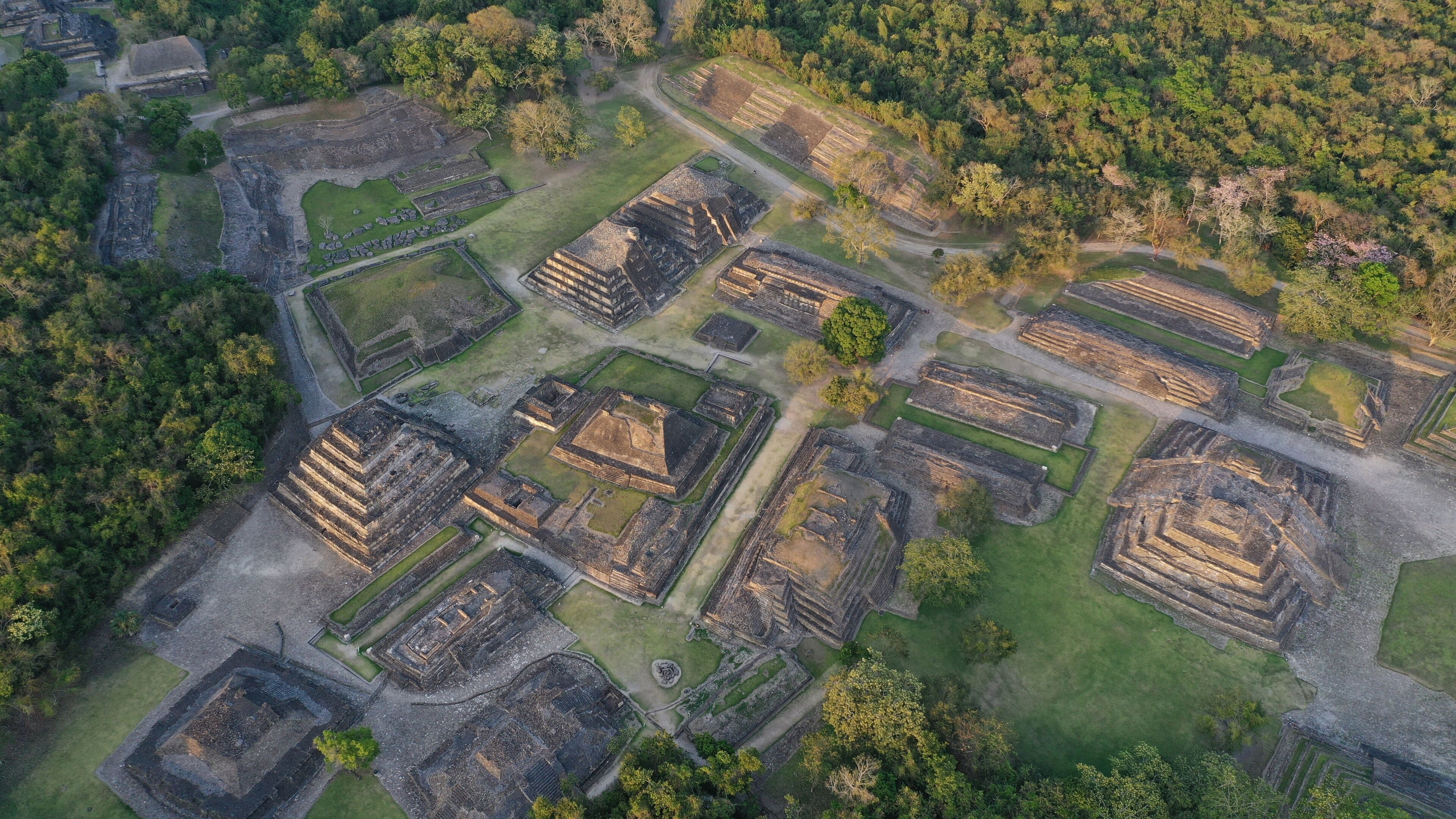 An aerial view of an ancient archaeological site with multiple rectangular structures and surrounding greenery.