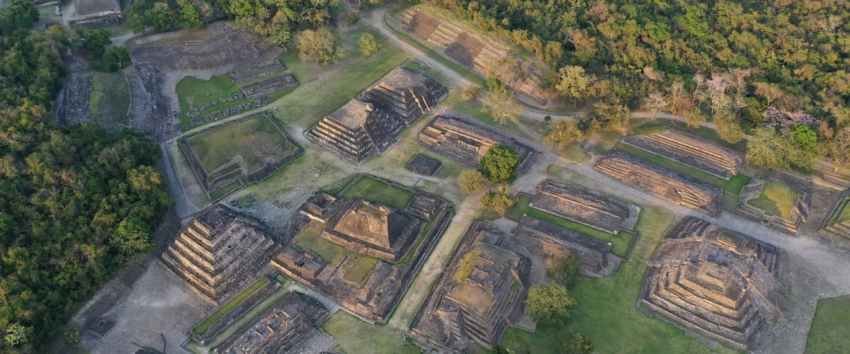 An aerial view of an ancient archaeological site with multiple rectangular structures and surrounding greenery.