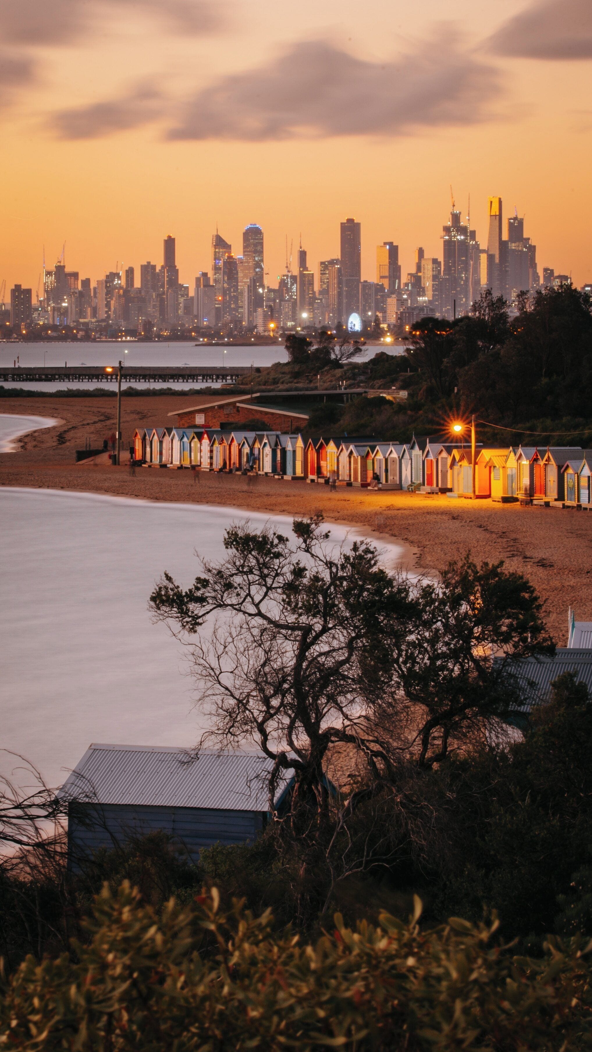 Brighton Beach sunset with colorful bathing boxes and Melbourne skyline in the background showcases natural beauty and urban charm in Victoria, Australia