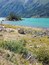 Paesaggio montuoso con un lago turchese, una riva rocciosa e vegetazione rada.