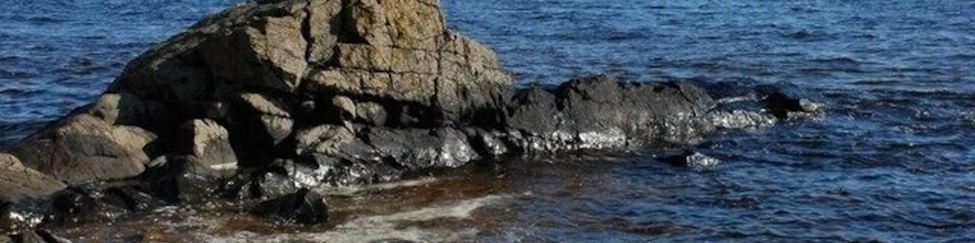 Uma costa rochosa com uma formação rochosa imponente e mar calmo.