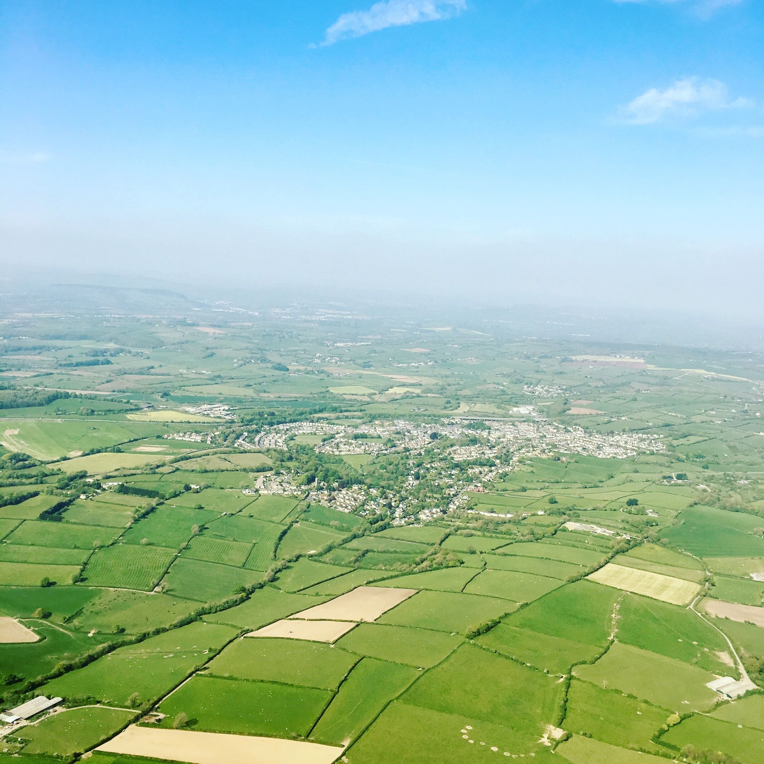 A rural landscape with fields, a small village, and rolling hills.