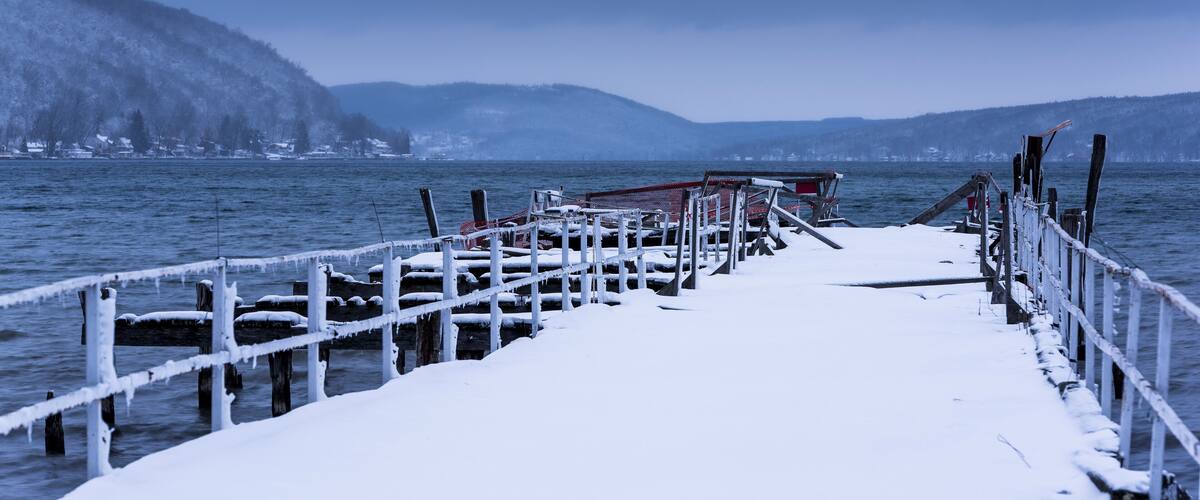 A snow-covered pier extending into a body of water, surrounded by hills and a clear sky.