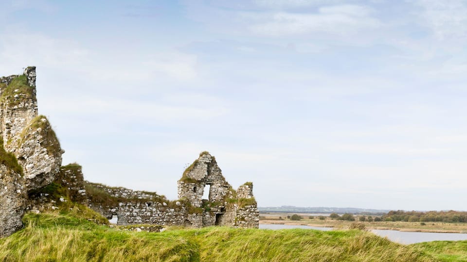 Ancient stone ruins with grass-covered walls and a river in the background.