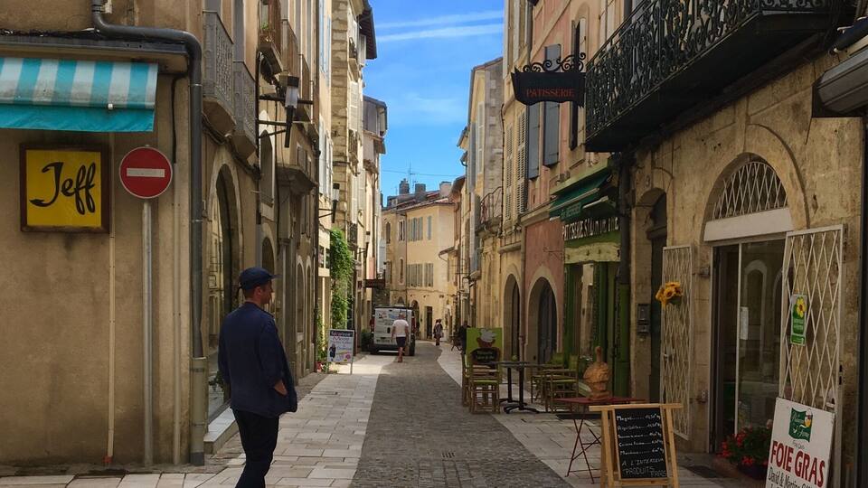 A cobblestone street lined with historic buildings, a man walking, and a bakery sign.