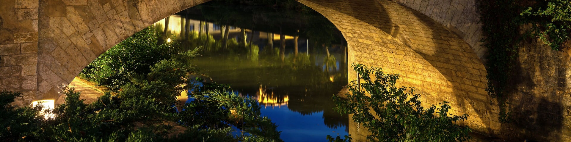 A stone bridge over a river with a castle in the background.