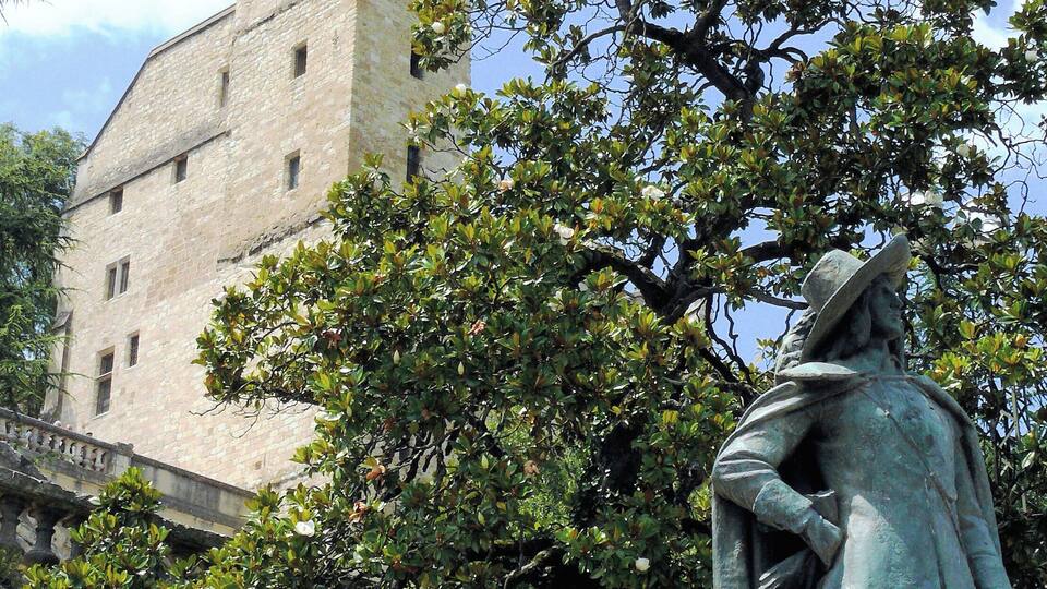A historic stone building with a tower and a statue of a man in period clothing.