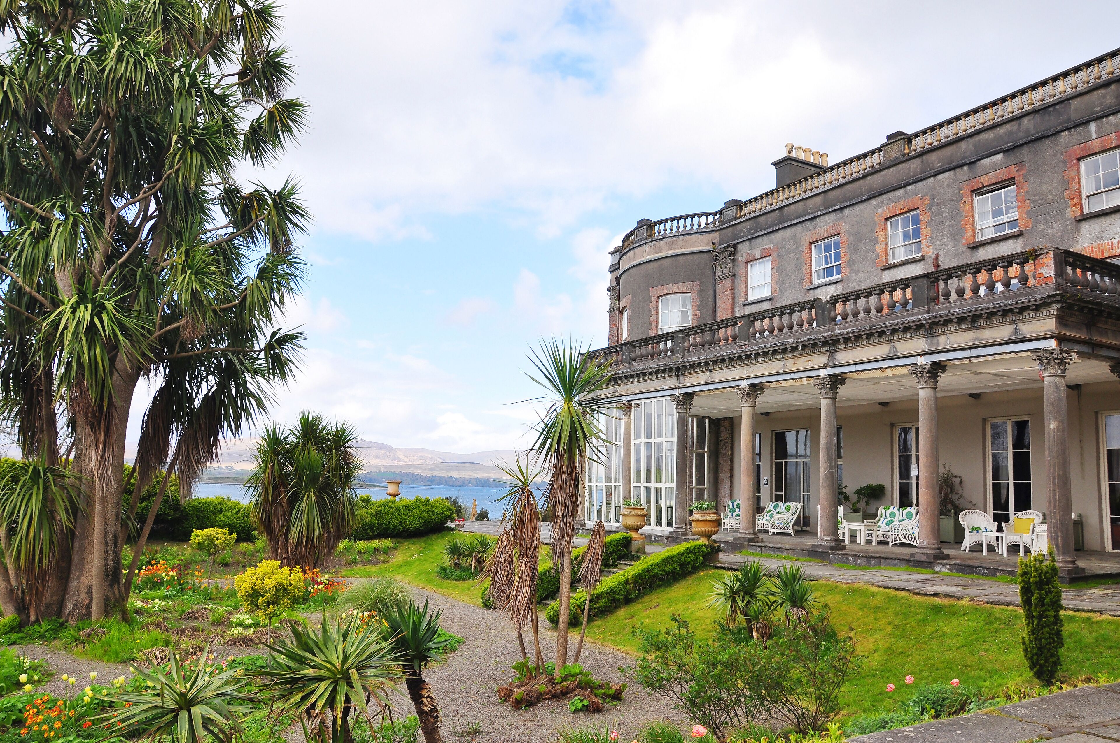 A grand building with a garden and a view of the sea.