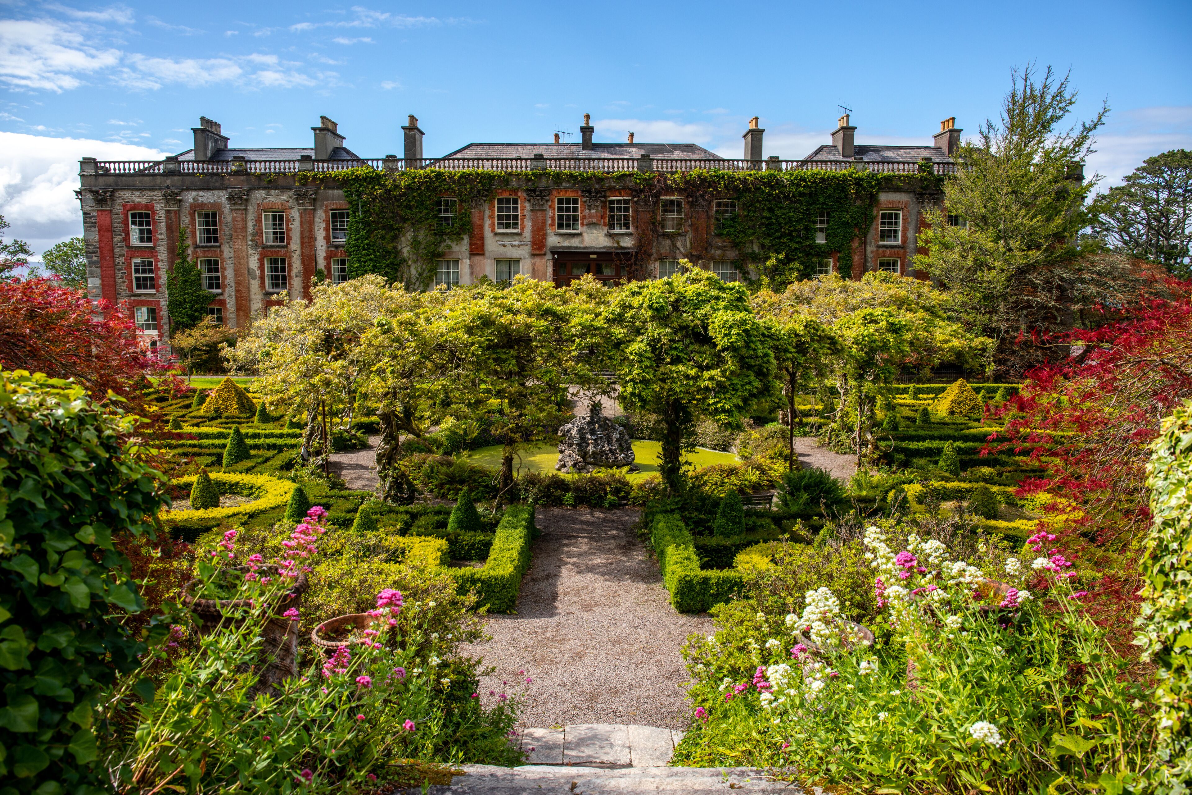 A historic building with a formal garden, including a central pathway and neatly trimmed hedges.