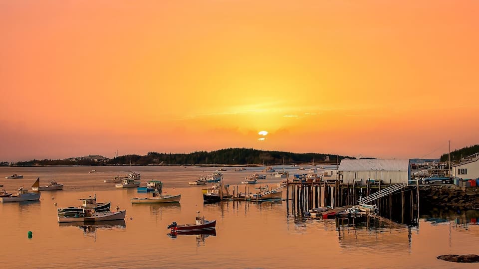 A harbor at sunset with boats, a pier, and buildings.