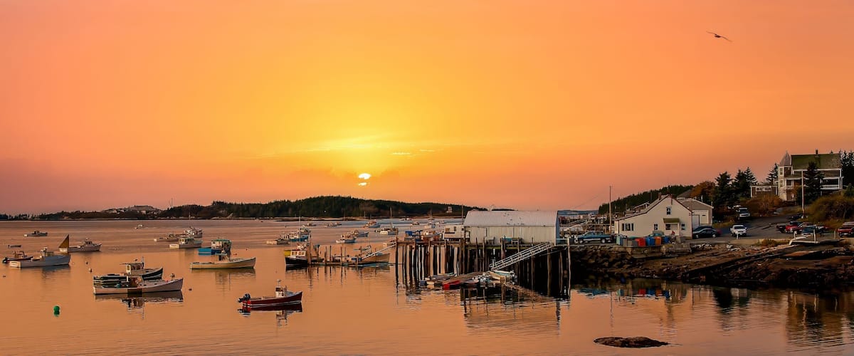 A harbor at sunset with boats, a pier, and buildings.