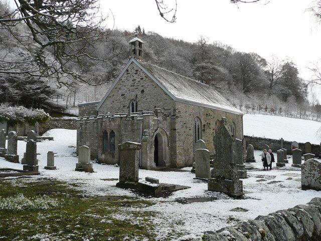 A church with a stone facade and arched windows, surrounded by snow-covered gravestones.