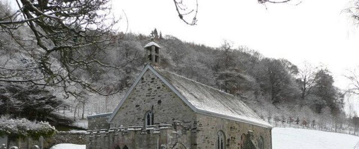 A church with a stone facade and arched windows, surrounded by snow-covered gravestones.
