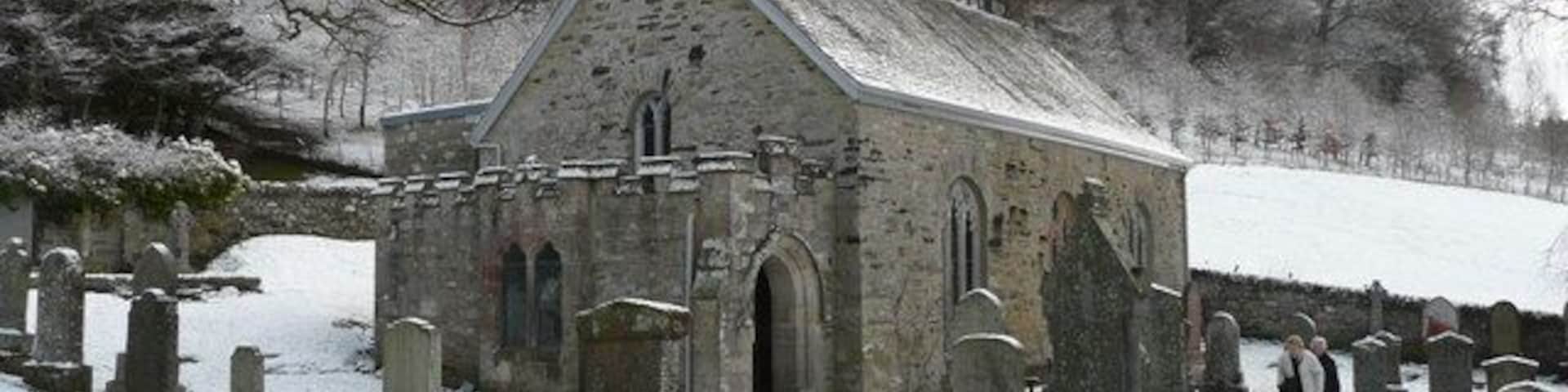 A church with a stone facade and arched windows, surrounded by snow-covered gravestones.