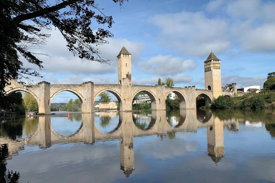 Un pont de pierre à arches multiples enjambant une rivière paisible, dont la structure et la végétation environnante se reflètent dans l’eau.