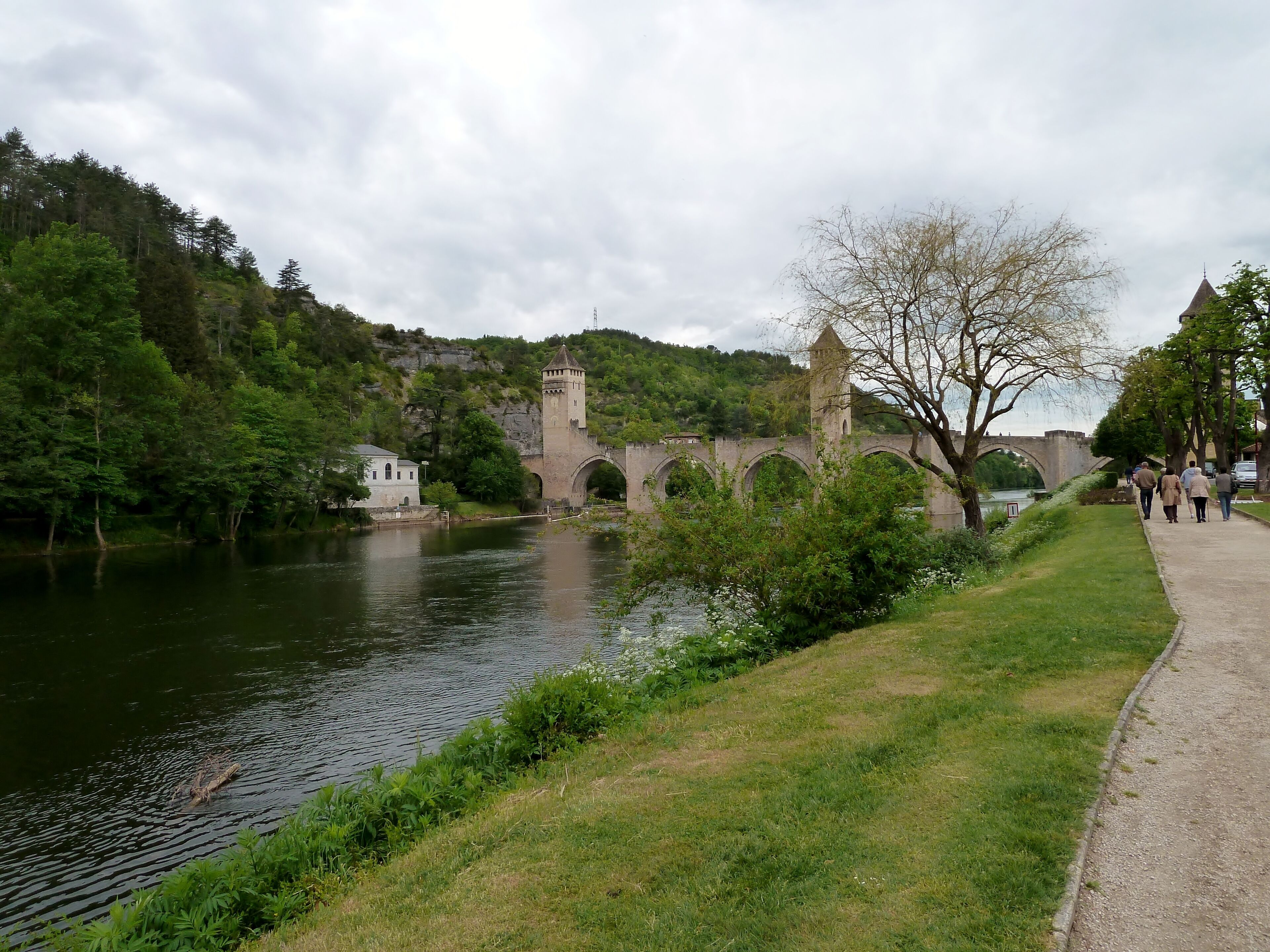 A stone bridge over a river, surrounded by lush greenery and a castle-like tower.