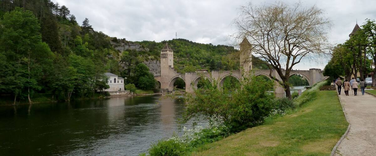 A stone bridge over a river, surrounded by lush greenery and a castle-like tower.