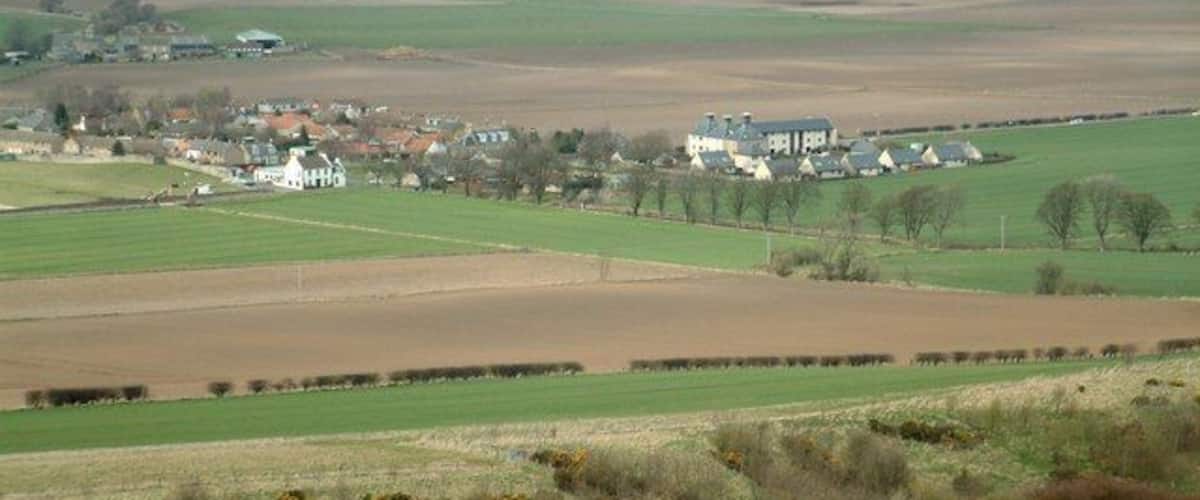 A rural landscape with fields, a small village, and a large white building.
