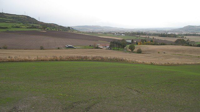 A rural landscape with fields, a small house, and distant hills.