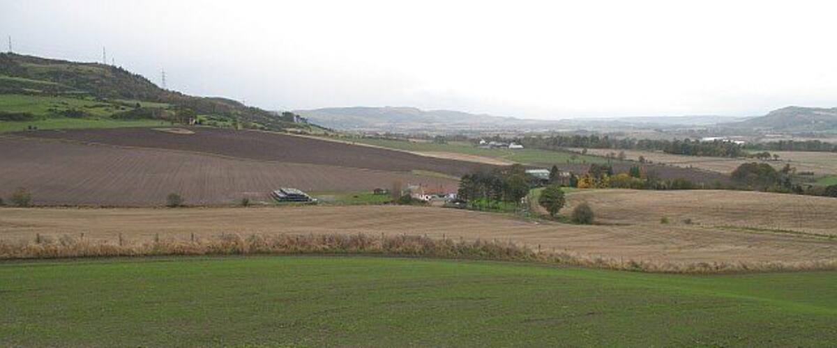 A rural landscape with fields, a small house, and distant hills.