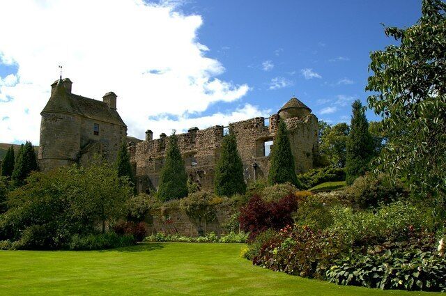 A historic castle with ruins, lush green lawns, and a variety of trees and shrubs.