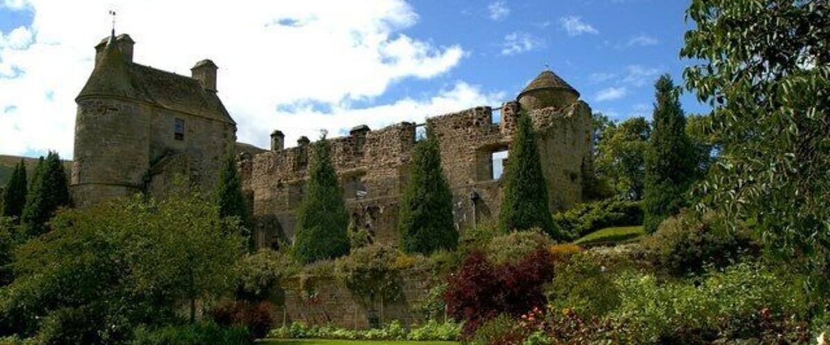 Un castillo histórico con ruinas, amplios jardines verdes y diversos árboles y arbustos.